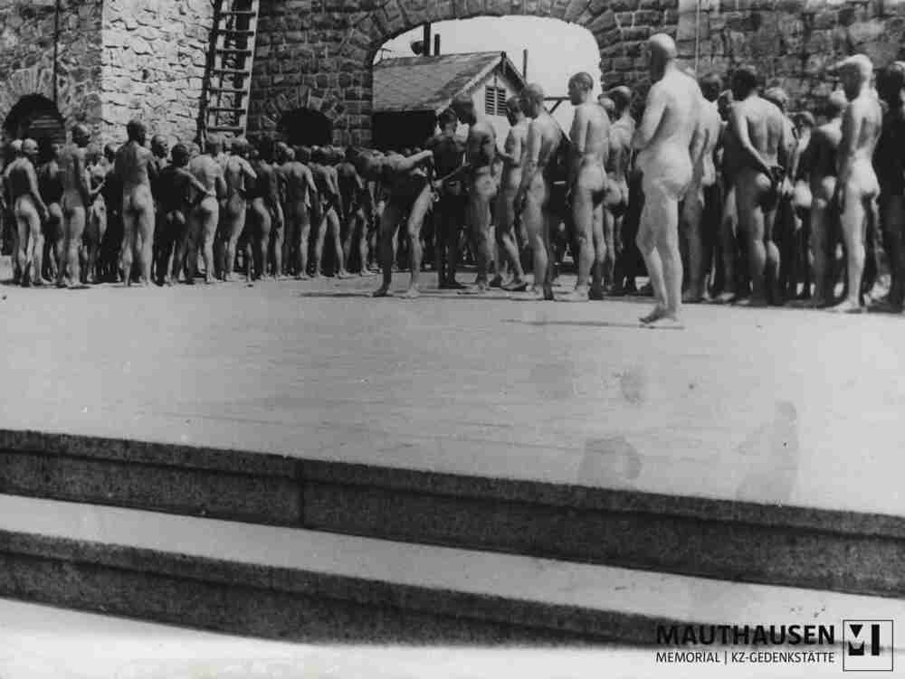 4.1.0587.jpg; 4.1.0587; SS-Erkennungsdienst im KZ Mauthausen: Nackte Häftlinge stehen in Reihen wartend am Lagertor / Jourhaus auf Desinfektion und ihre entlauste Kleidung in Folge einer Fleckfieberepidemie im Sommer 1941; siehe auch 4.1.0586 - 4.1.0586.2 sowie 4.1.0587 - 4.1.0587.3;