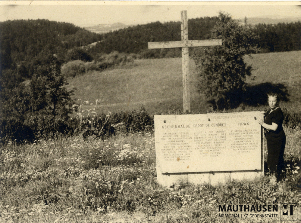 MM_4_15_015.jpg; 4.15.015; KZ Gedenkstätte Mauthausen: Miriam Novitch steht seitlich neben einem Gedenkstein und Kreuz. Das Mahnmal kennzeichnet die sogenannte Aschenhalde. ; Fotografie