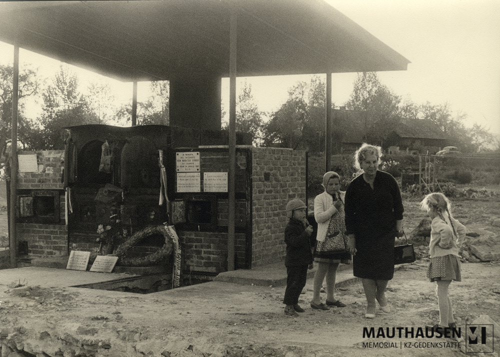 MM_4_15_018.jpg; 4.15.018; Areal des ehemaligen Konzentrationslagers Gusen: Miriam Novitch steht neben den Überresten des Krematoriums, das als inoffizielle Gedenkstätte fungiert, umringt von Kindern aus der Umgebung. ; Fotografie