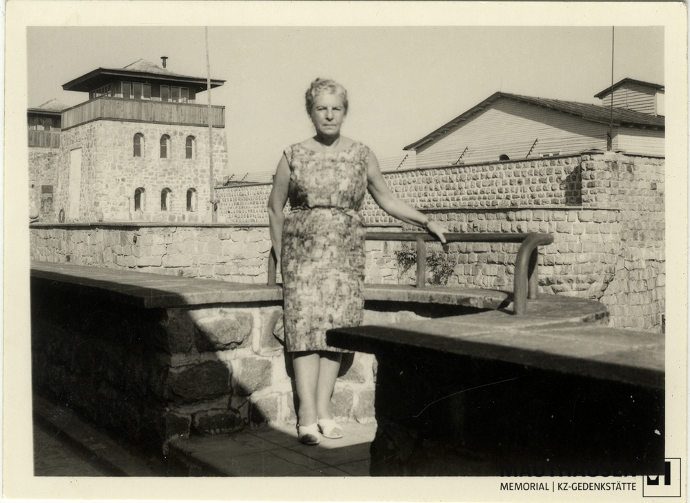 MM_4_15_021.jpg; 4.15.021; KZ Gedenkstätte Mauthausen: Miriam Novitch steht auf einem Balkon vor dem ehemaligen SS-Kommandaturgebäude. Im Hintergrund der Eingang zum Lager, sowie Teile der Lagermauern.; Fotografie